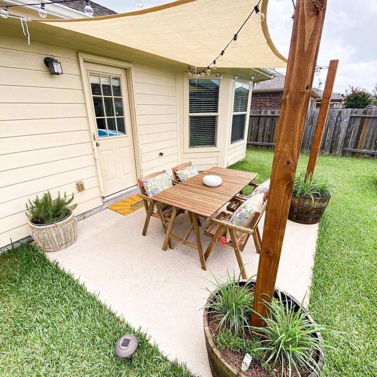 a patio with a table and chairs under an awning next to a fenced in back yard