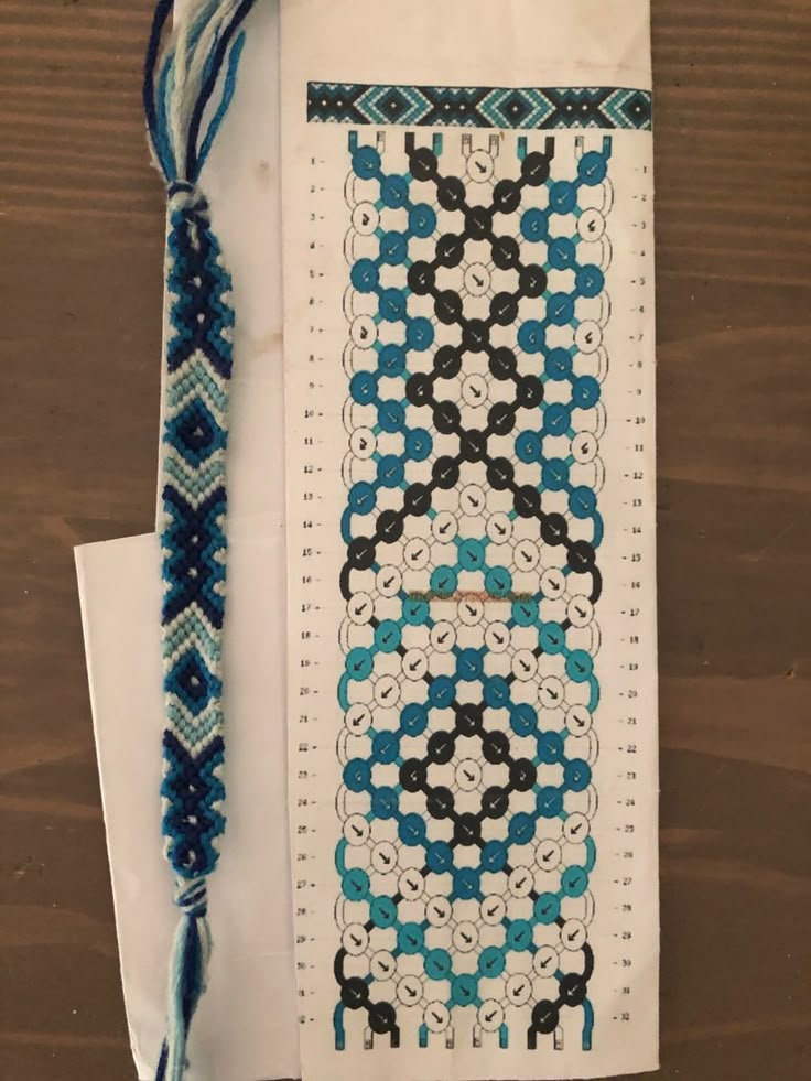 a cross stitch bookmark with blue and black designs on it next to a tassel