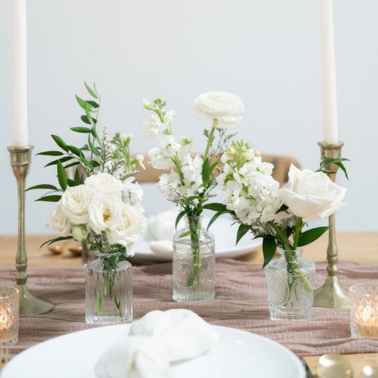 white flowers in glass vases on a table with silverware and candlesticks