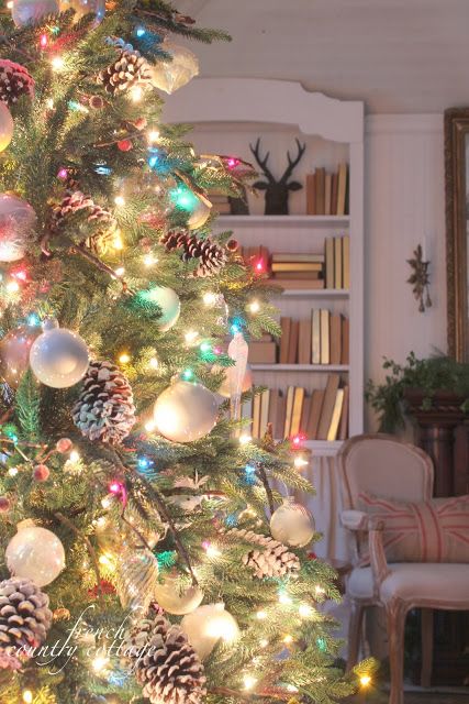 a decorated christmas tree in a living room with lights on and pine cones hanging from the branches