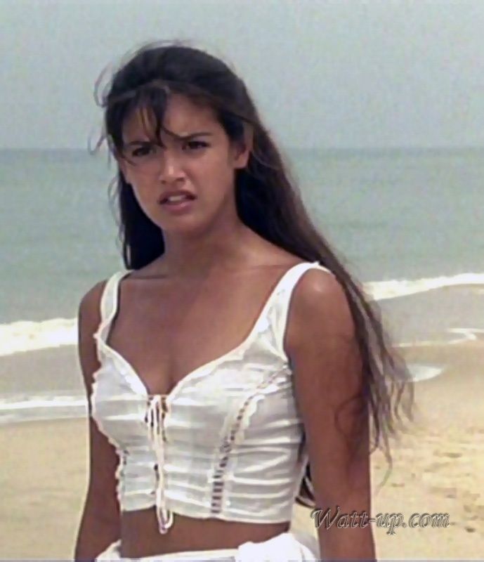 a woman standing on top of a sandy beach next to the ocean with her hair blowing in the wind