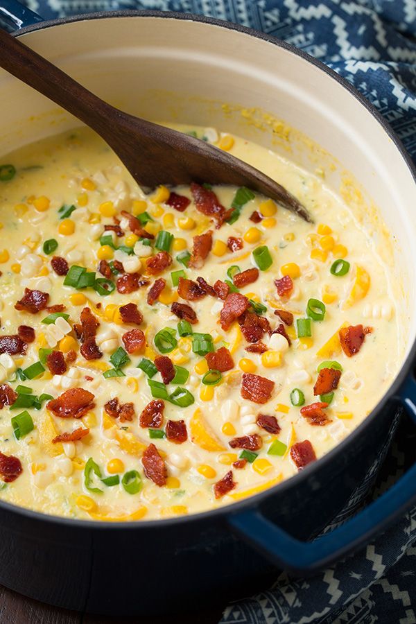 a pot filled with corn and bacon on top of a blue cloth next to a wooden spoon