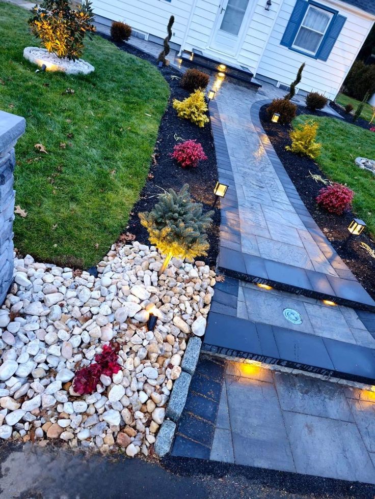 an outdoor walkway lit up with lights in the grass and rocks on both sides, leading to a house