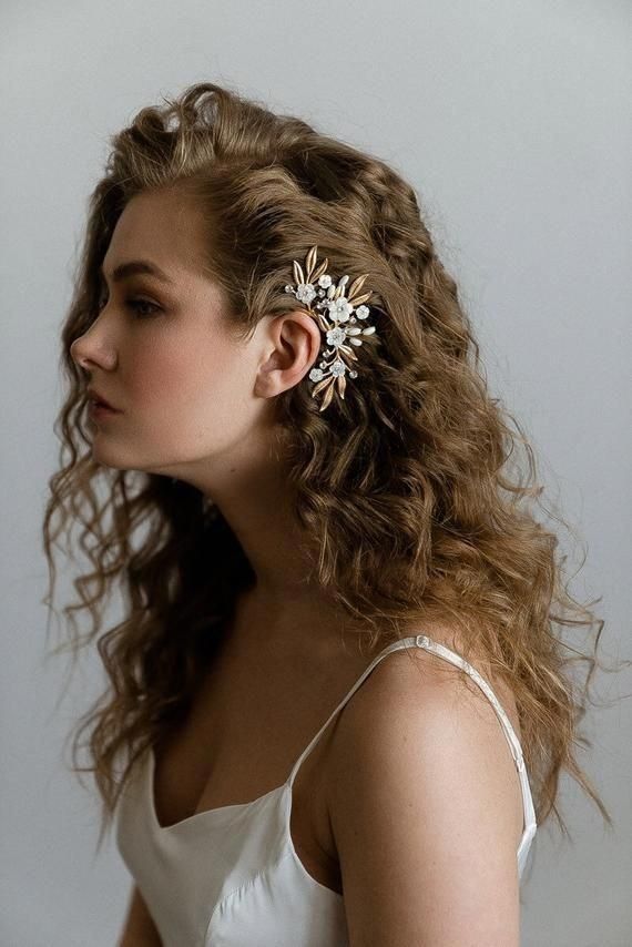 a woman with long curly hair wearing a white dress and a gold flower brooch