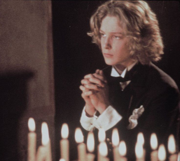 a young man standing in front of a bunch of lit candles with his hands clasped