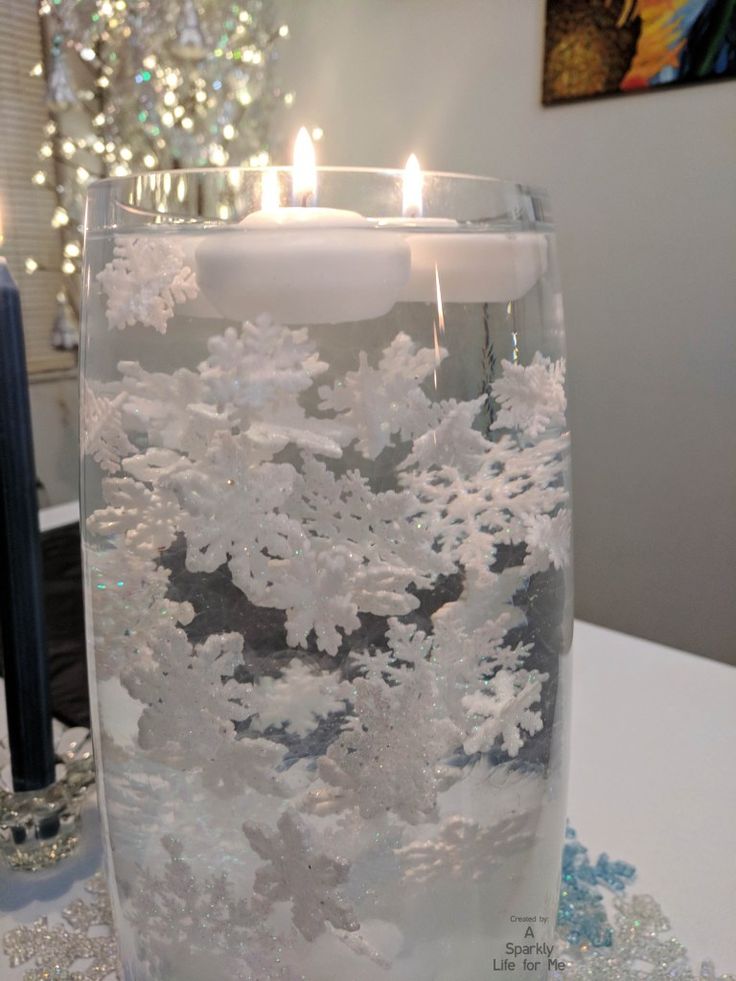 a candle that is inside of a glass with snow flakes on it and some candles in the background