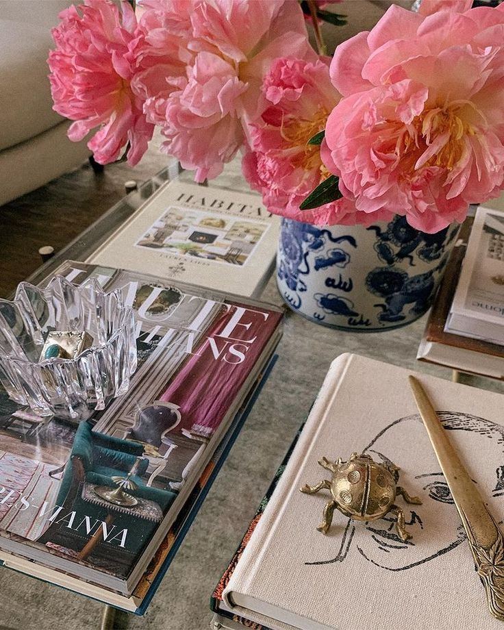 pink flowers are in a blue and white vase next to books on a coffee table