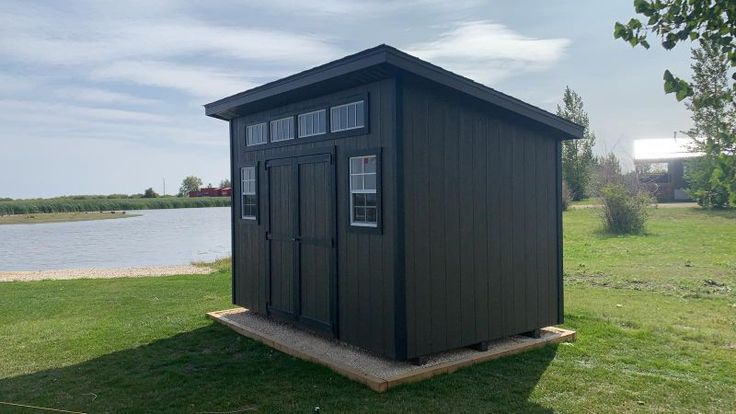 a small black shed sitting on top of a lush green field next to a lake