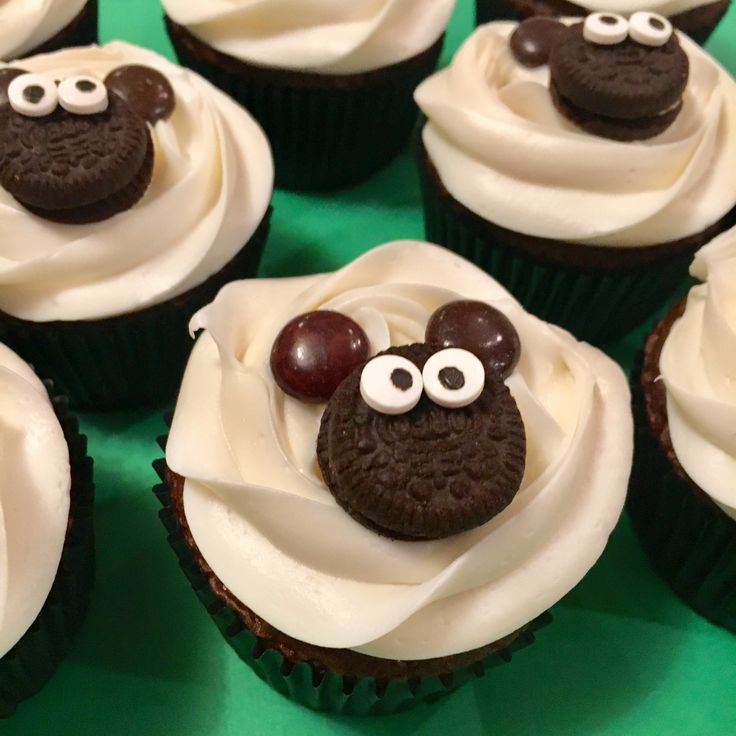 cupcakes decorated with white frosting and chocolate decorations are displayed on a green surface