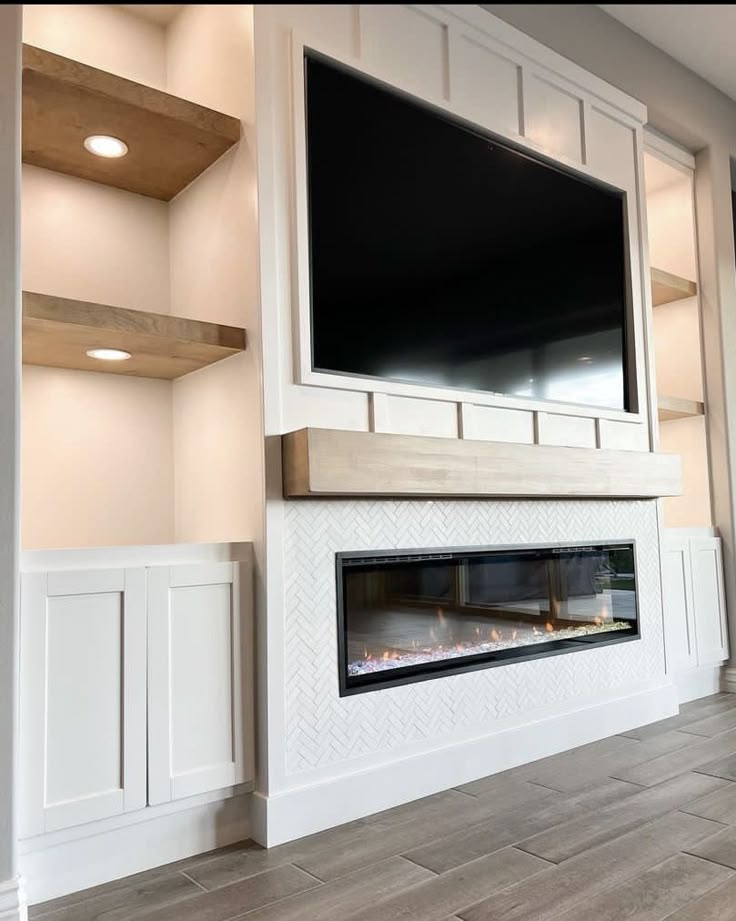 an empty living room with a large flat screen tv mounted above the fireplace and built - in shelving