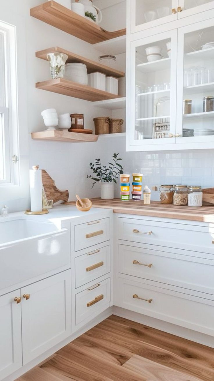 a kitchen with white cabinets and wooden floors is pictured in this image, there are shelves on the wall above the sink