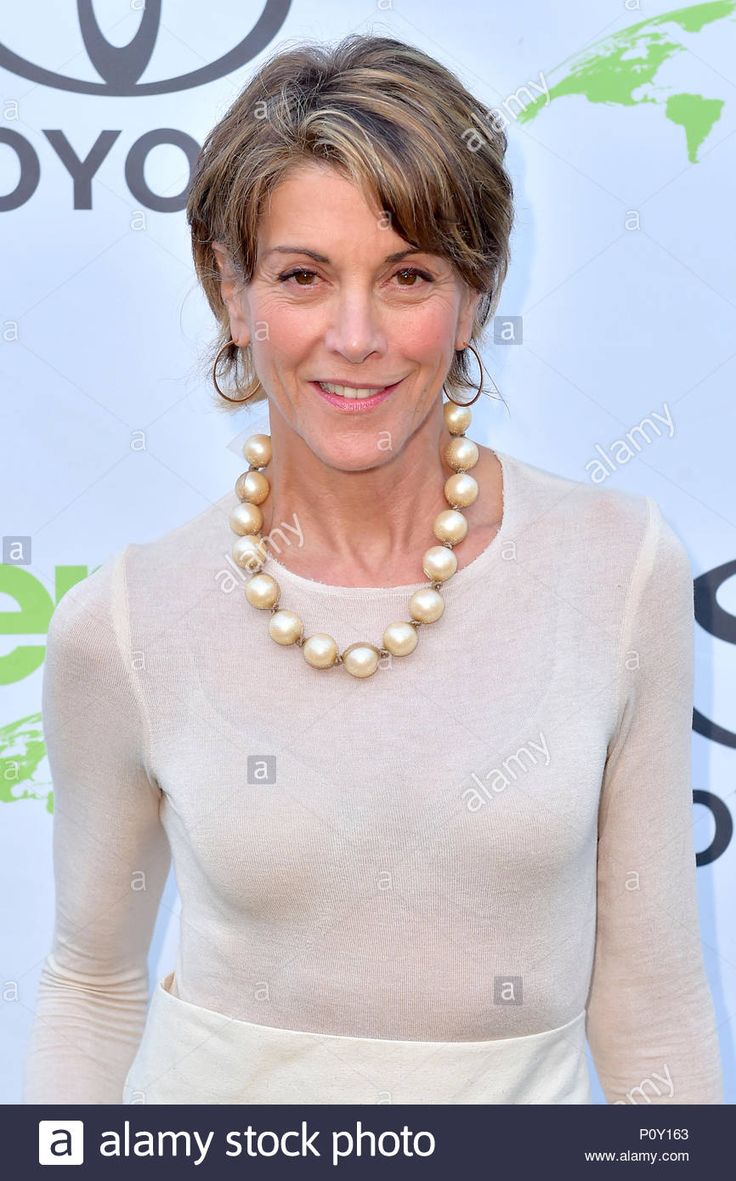 an older woman with short hair wearing a white dress and pearls necklace, smiling at the camera