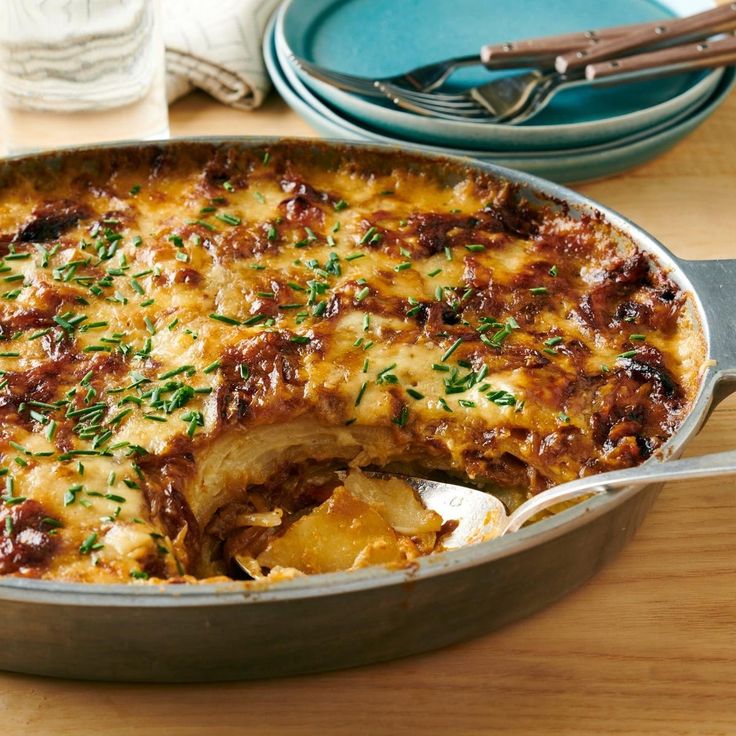 a casserole with meat and cheese in a pan on a table next to plates