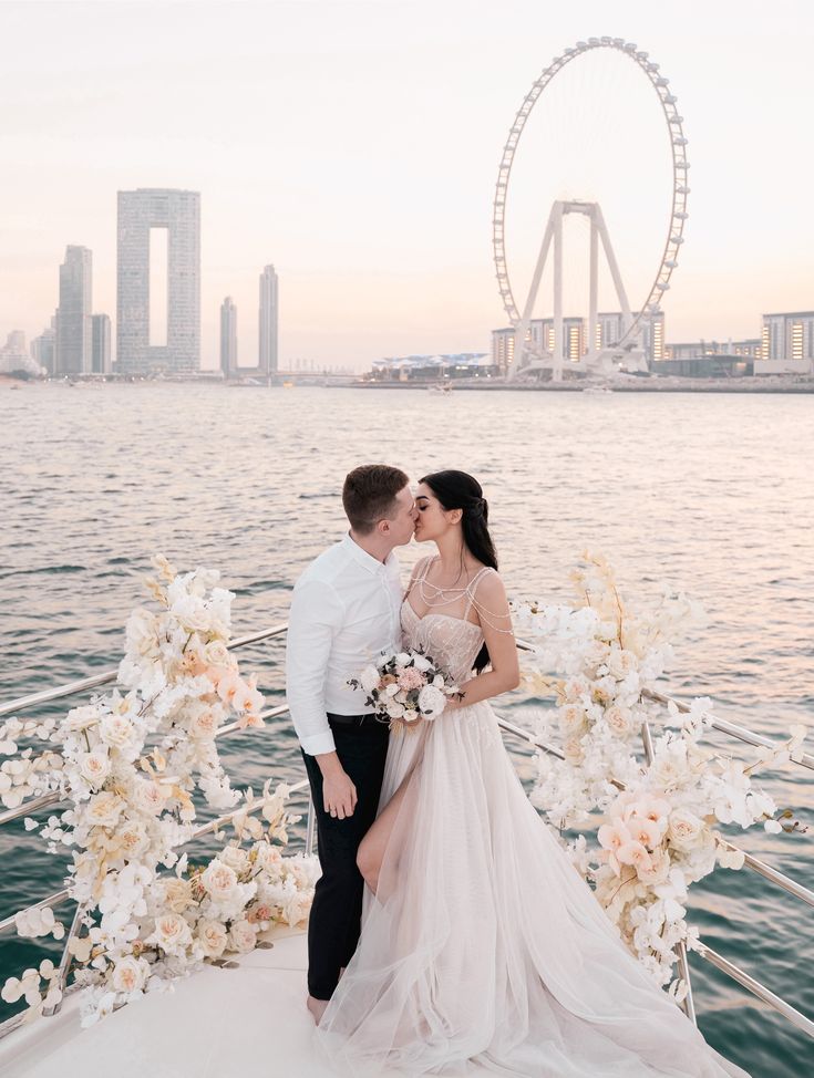 a bride and groom kissing on the back of a boat in front of a ferris wheel