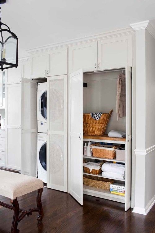 an open closet with white cabinets and baskets on the door, in a room with hardwood floors