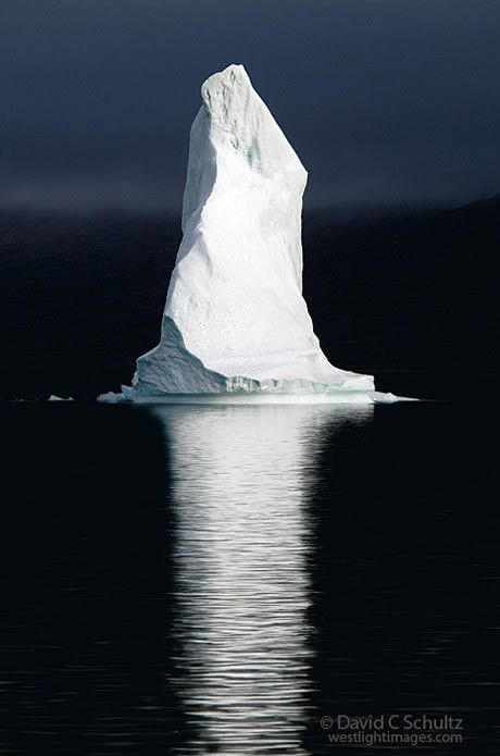 an iceberg floating in the middle of the ocean with dark skies above it and water reflecting on the surface