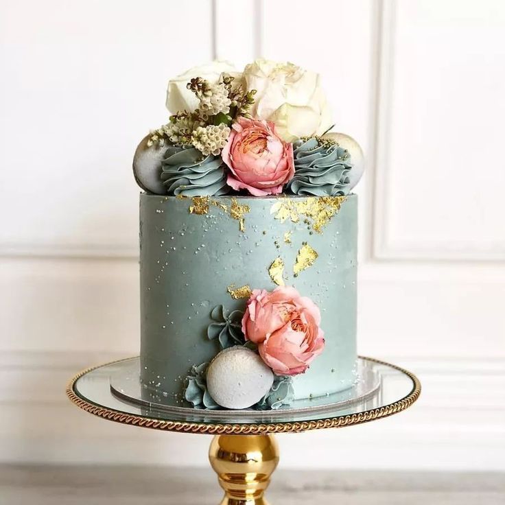 a blue and gold cake with flowers on top sitting on a table next to a white wall