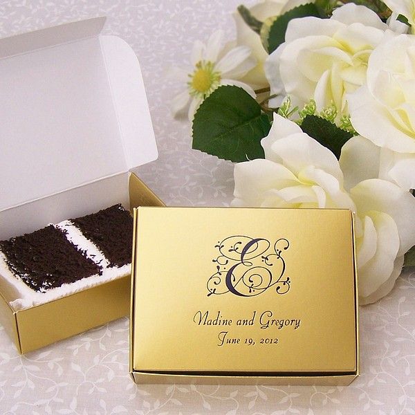 a wedding cake in a gold box next to white flowers on a lace tablecloth