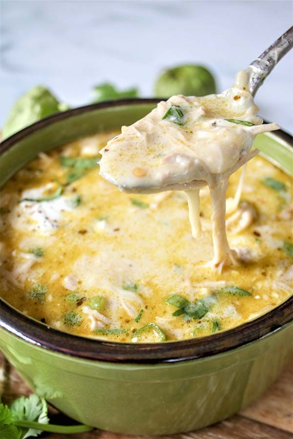 a spoon full of soup with broccoli and cheese on it, being lifted from a green bowl