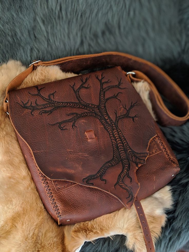 Twisted Tree Leather Satchel This bag is SOLD. We will lovingly craft a similar, yet unique one just for you. We will incorporate the beautiful, natural edges of the hide. This bag is made out of kodiak stone oil leather. It is full of wonderful color variations and is incredibly durable and water resistant. This bag is adorned with a freehand pyrographic drawing of a twisted, gnarly, old tree. It is hand stitched with nylon waxed thread. The stress points are reinforced with antique brass rivet Hand Tooled Leather Bag, Unique Leather Bag As A Gift, Artisan Leather Saddle Bag With Leather Lining, Leather Bags For Everyday Use, Artisan Leather Satchel, Everyday Leather Shoulder Bag, Rustic Hand Tooled Bag For Everyday Use, Unique Hand-stitched Bags For Everyday Use, Nature-inspired Handmade Shoulder Bag For Everyday Use