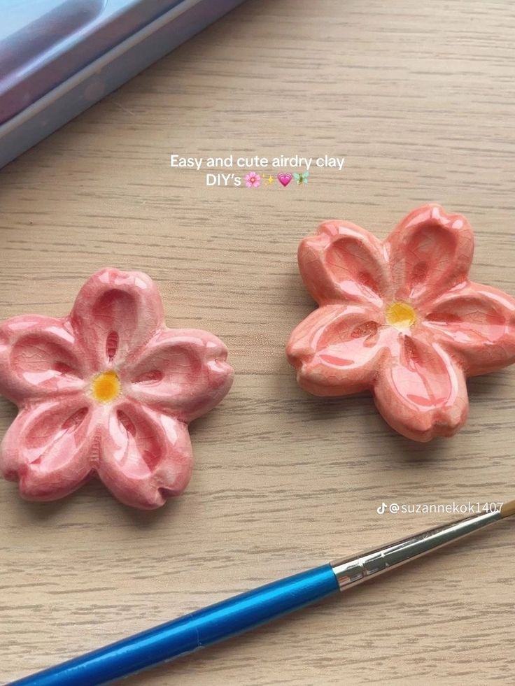 two pink flowers sitting on top of a wooden table next to a blue marker and pen