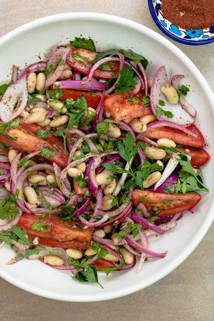 a white bowl filled with red onions, beans and greens on top of a table