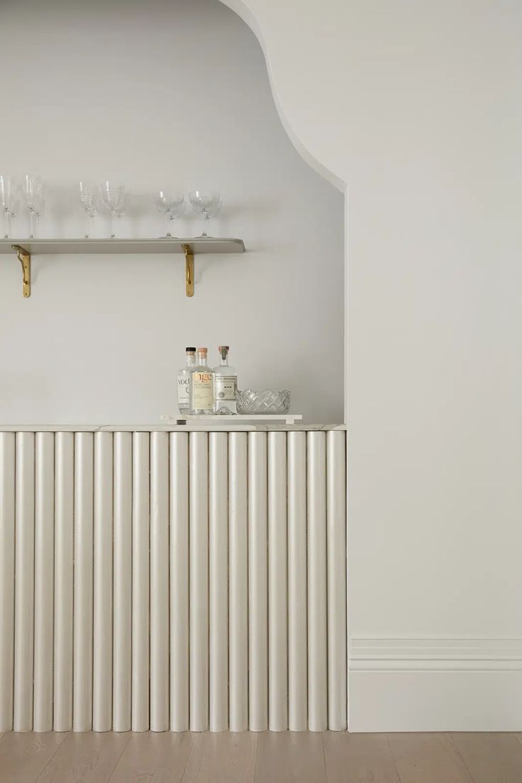 an empty room with white walls and wooden flooring, shelves on the wall are filled with wine glasses