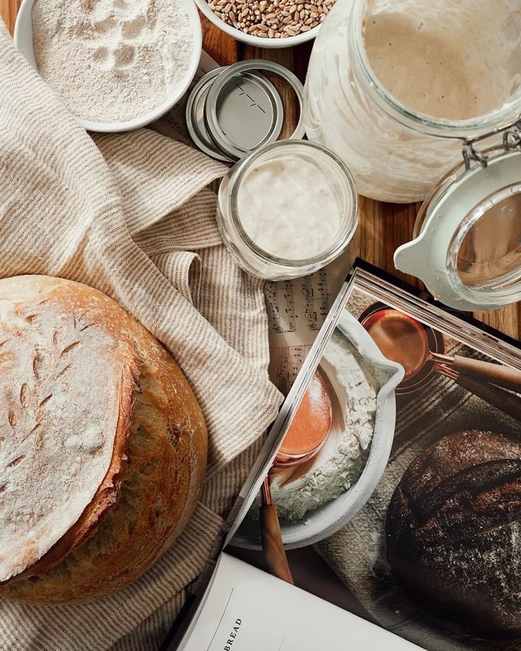 bread, flour and other baking ingredients on a wooden table with an open cookbook