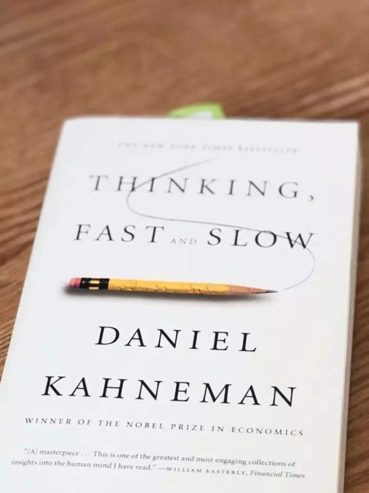 the book thinking, fast and slow by daniel kahneman on a wooden table