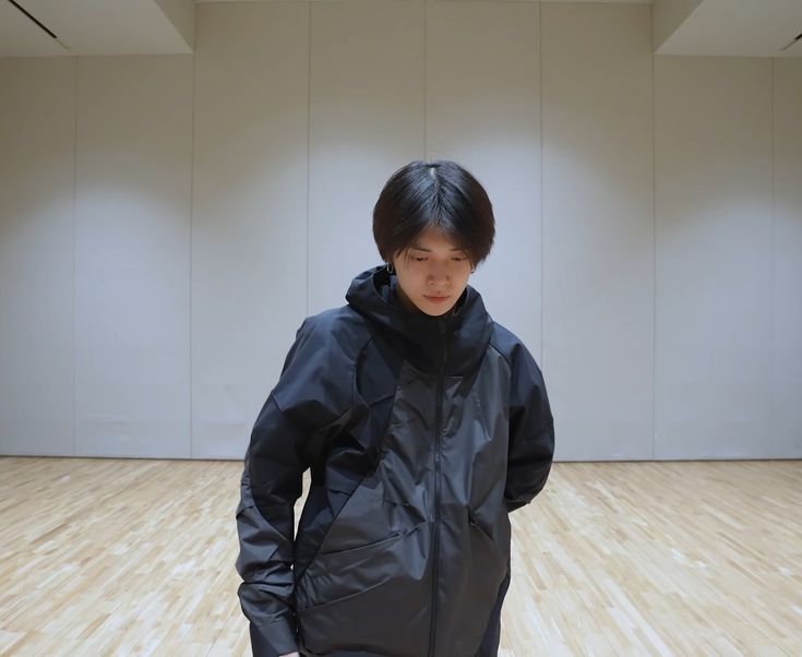 a young man standing in an empty room wearing a black jacket and pants with his hands on his hips