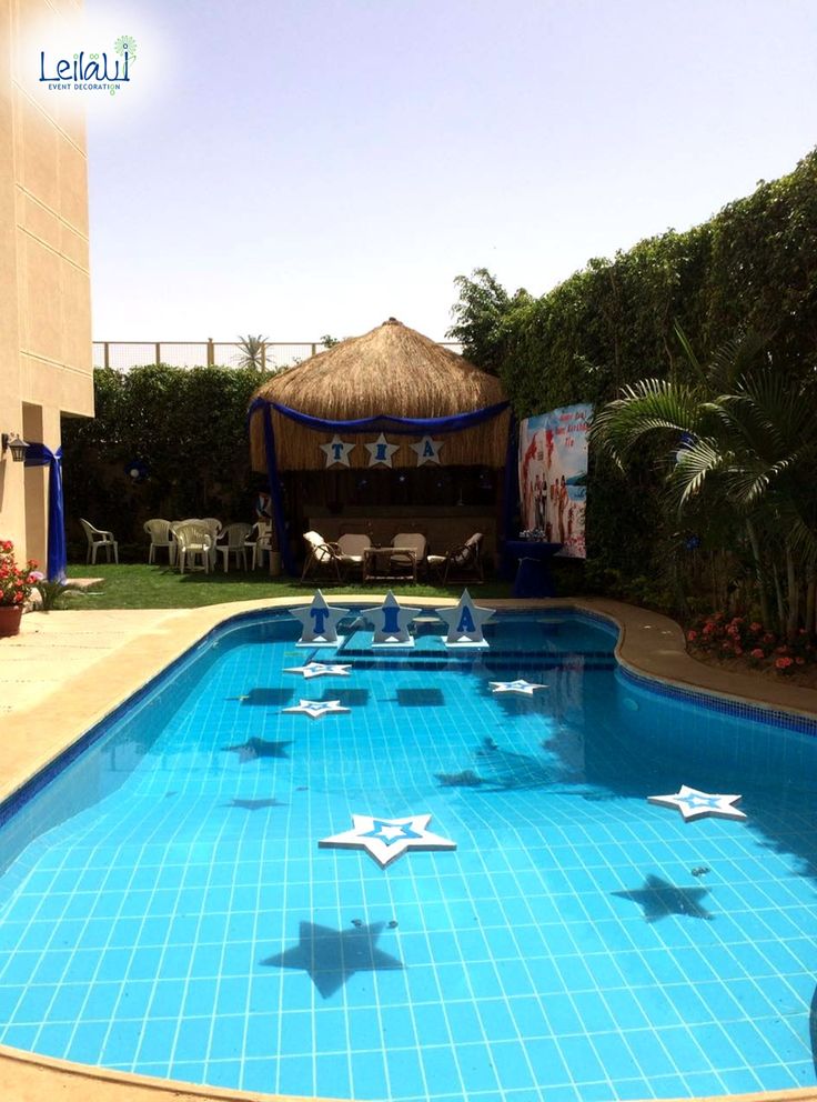 an empty swimming pool with blue tiles and white stars on the bottom, in front of a tiki hut