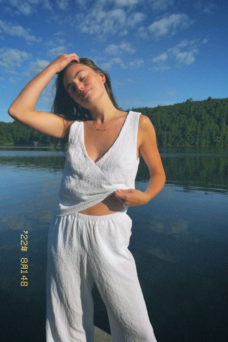 a woman standing on the edge of a body of water with her hands behind her head