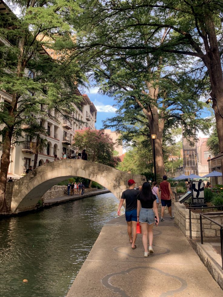 two people walking down a sidewalk next to a river