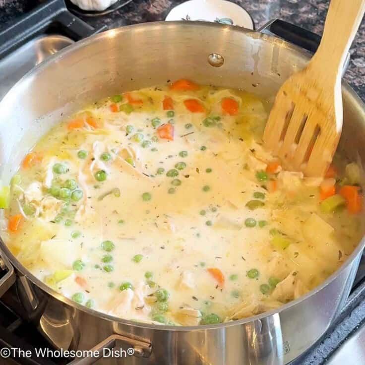 a pot filled with chicken and vegetables on top of a stove next to a wooden spoon