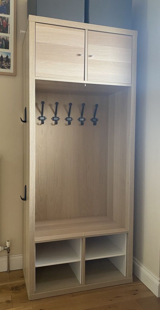 a wooden locker with several hooks on the door and two shelves below it in a living room