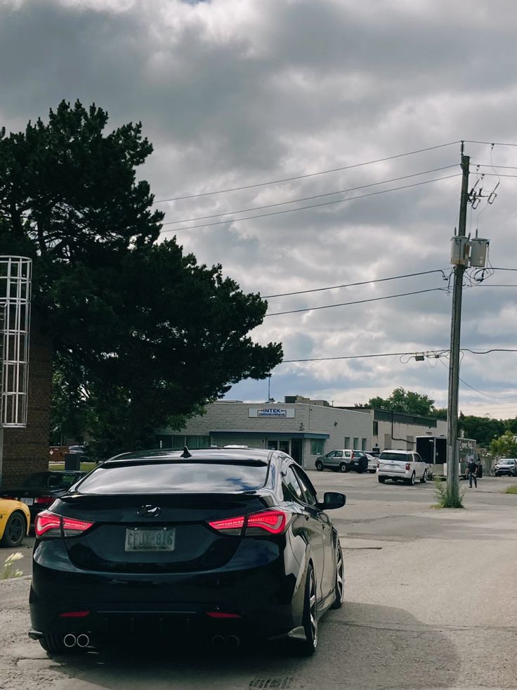 a black car parked on the side of a road next to a yellow car and some power lines