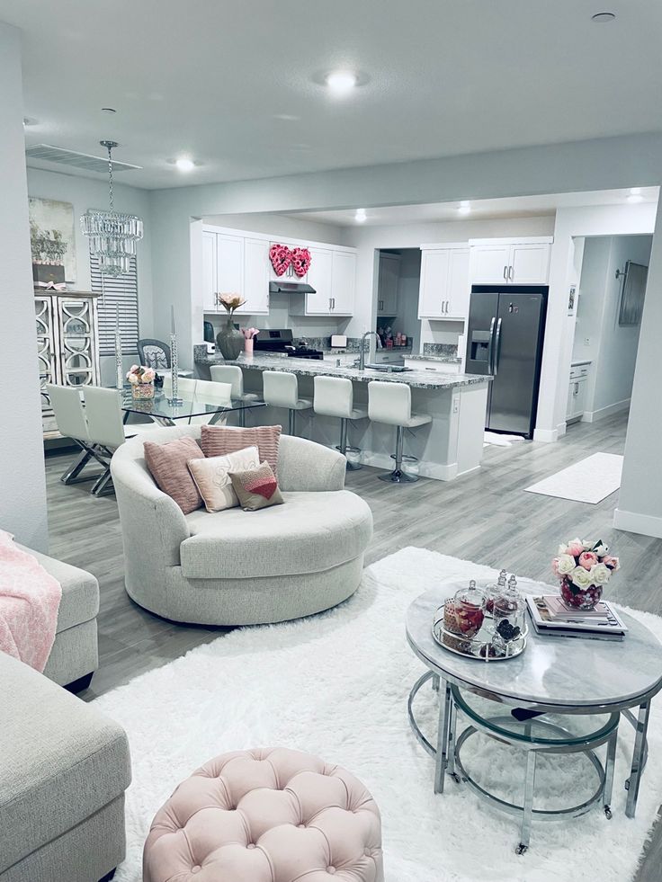 a living room filled with lots of furniture and white carpeted flooring in front of a kitchen