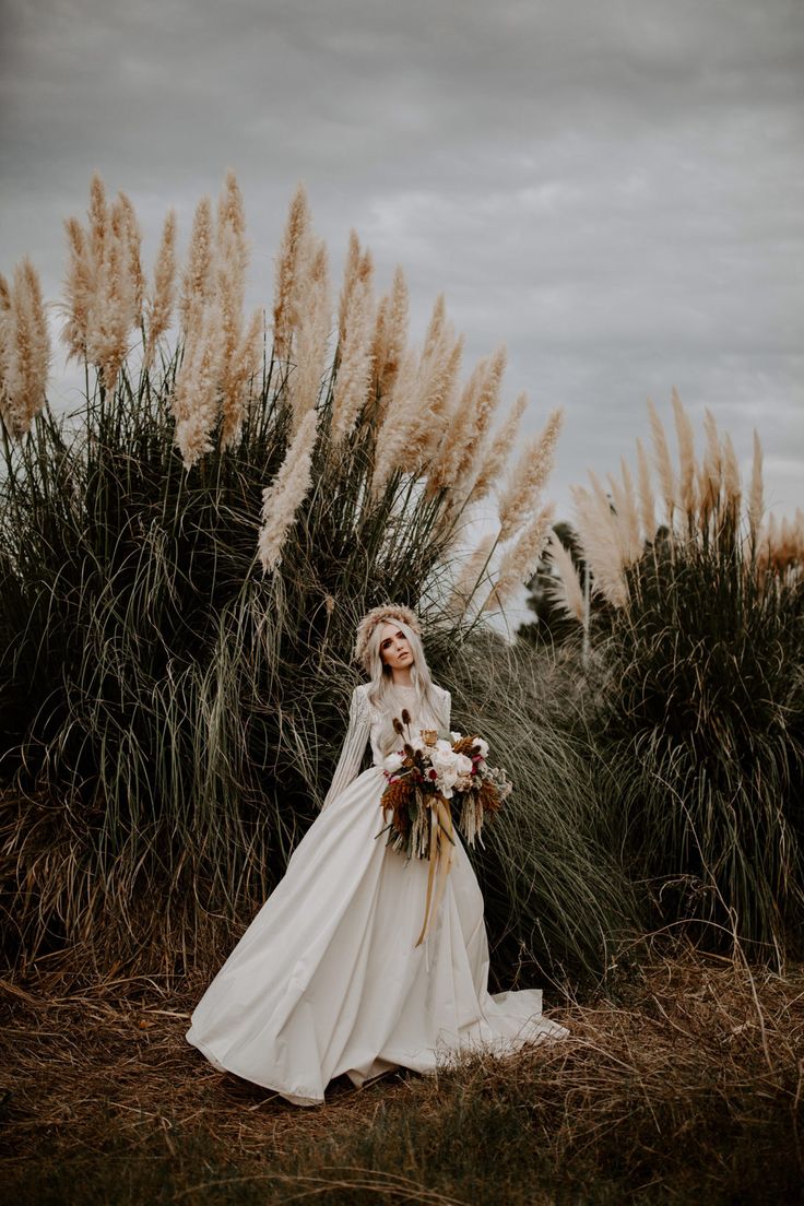 a woman in a wedding dress standing next to tall grass