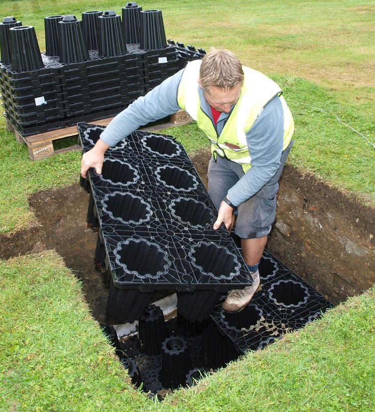 a man is placing black tiles into a hole in the ground to be used for drainage