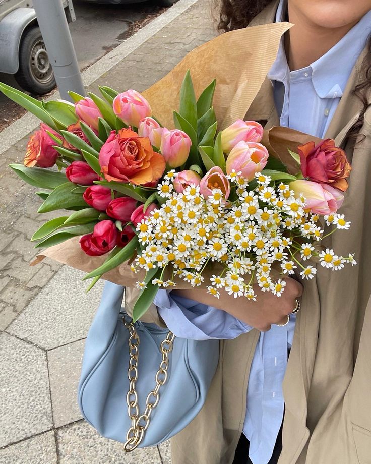 a woman holding a bouquet of flowers in her hand on the sidewalk near some cars