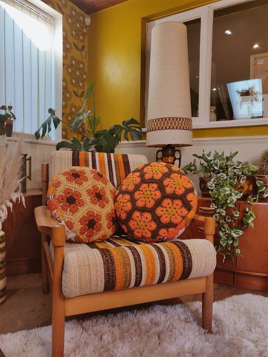 a chair with two pillows on it in front of a lamp and potted plants