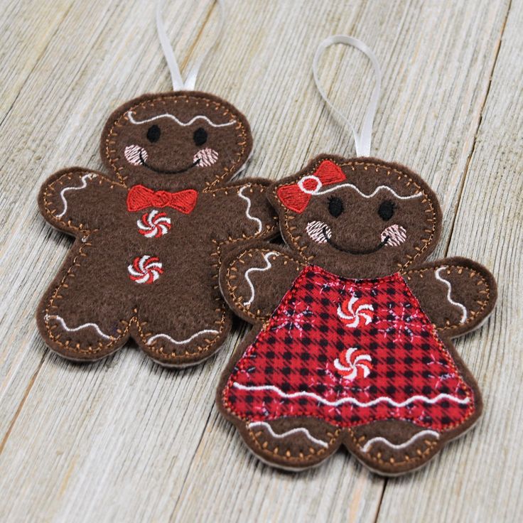 two brown gingerbread cookies with red and white checkered dresses hanging from strings on wooden surface