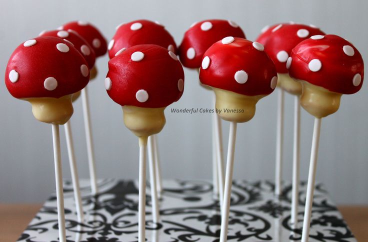 cake pops with red and white mushrooms on them sitting on a black and white tablecloth