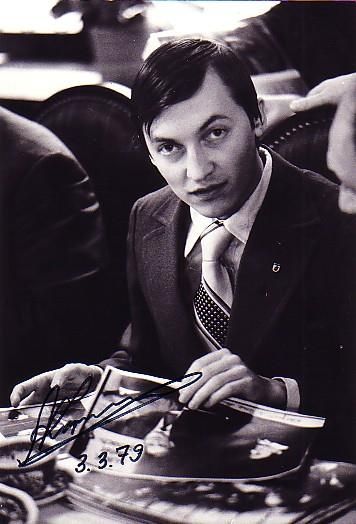 a black and white photo of a man in a suit signing autographs at a desk