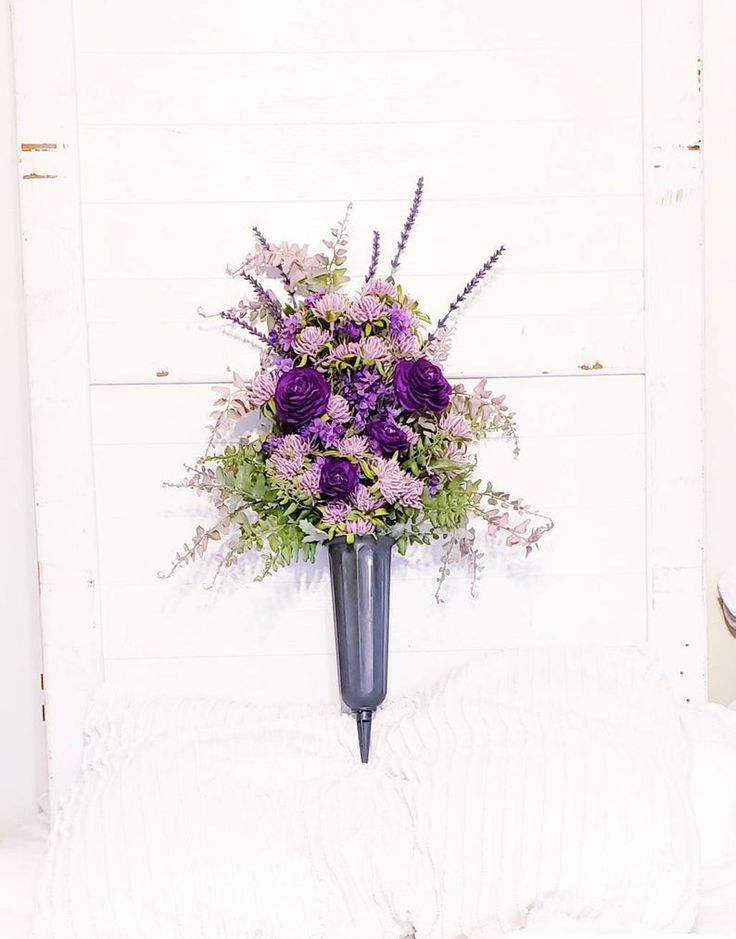 a purple flower arrangement in a black vase on a white bed with sheets and pillows