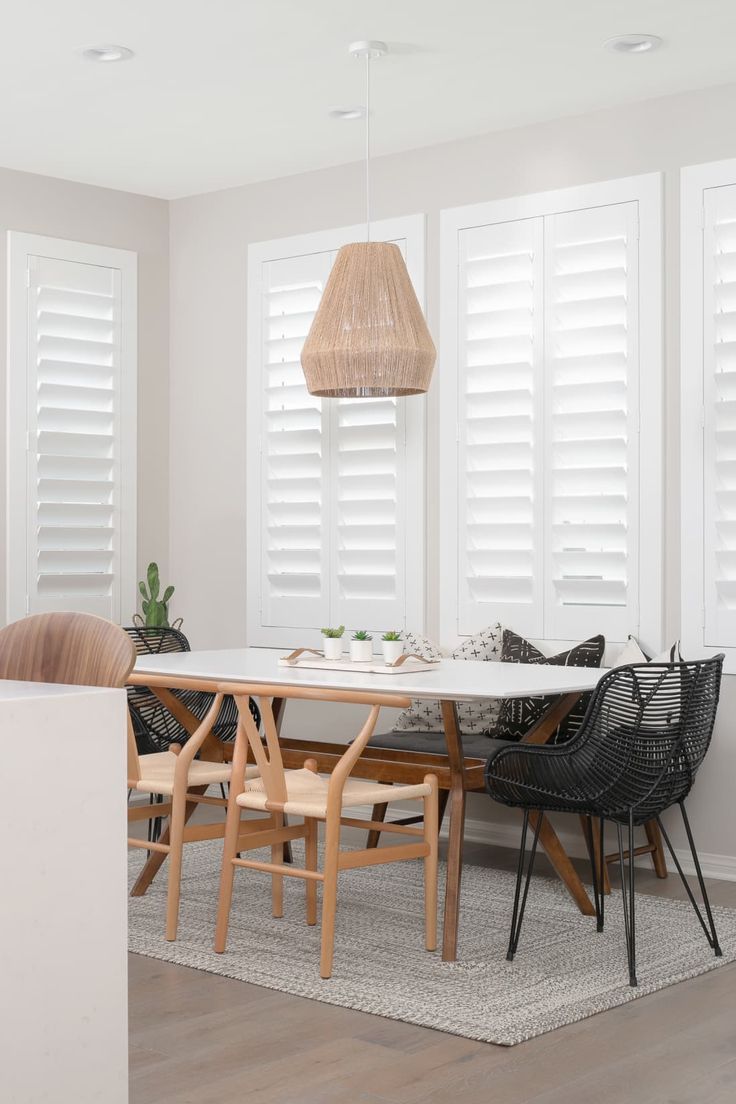 a dining room with white shuttered windows and wooden chairs in front of the table