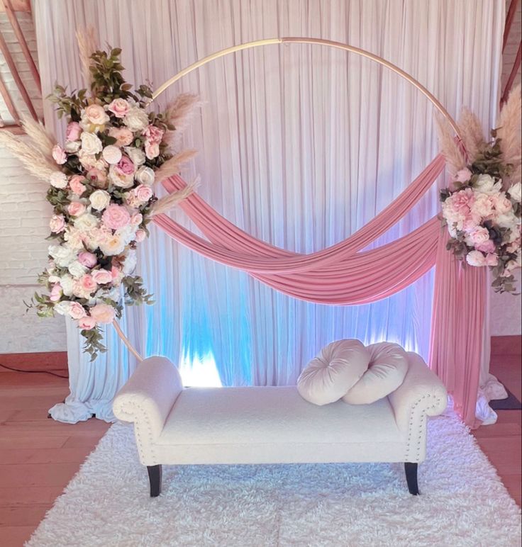 a white couch sitting under a pink and white arch with flowers on it's side