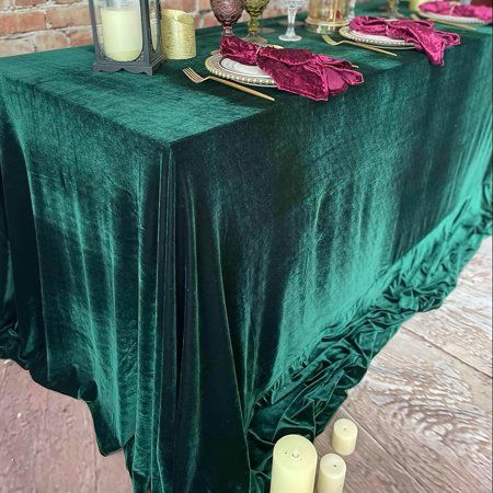 the table is set with candles, plates and napkins on it's green cloth