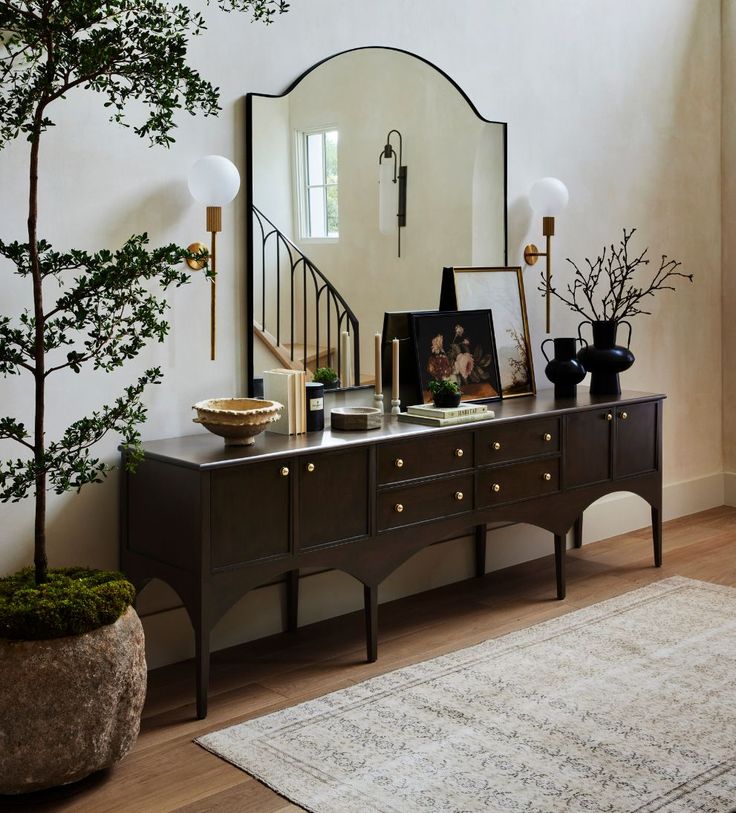 a living room with a large mirror on the wall next to a dresser and potted tree