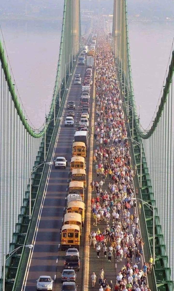 a large group of people walking across a bridge with buses and cars on the road